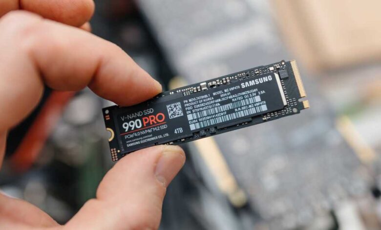 Man holding Samsung 990 PRO SSD between fingers over exposed laptop hero
